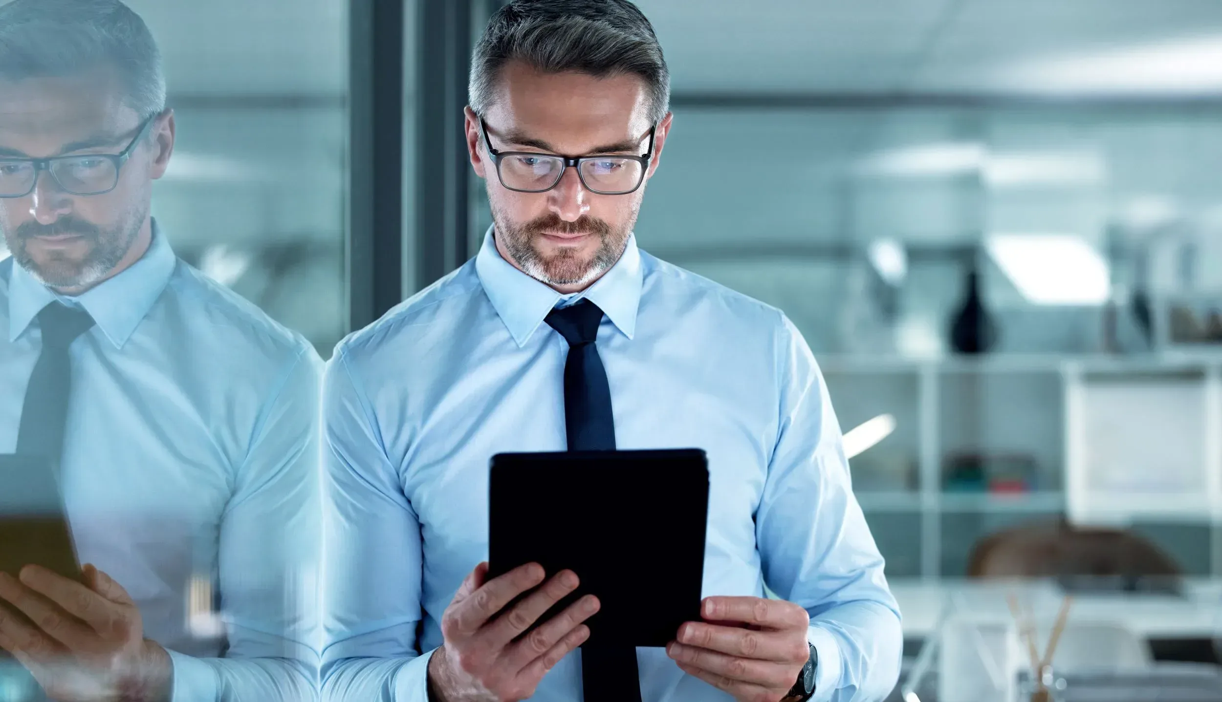 Lawyer in business casual dress leaning against glass wall with tablet in hand