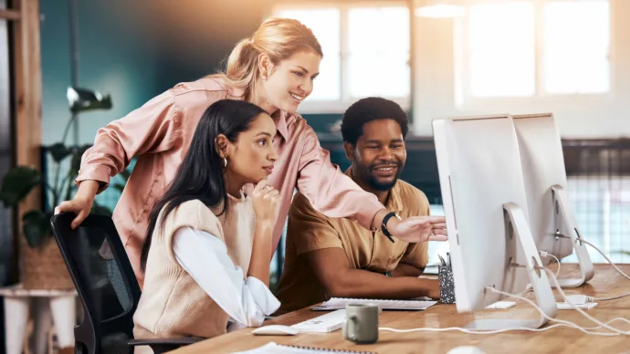 Three professionals stand around a computer with an amber glow in the background