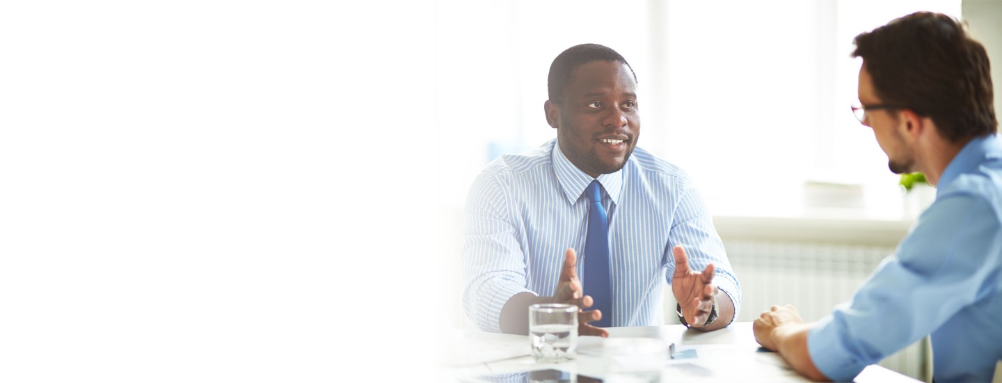 2880x1100 left white gradient of an Afro-American bearded HR manager sitting at office desk while conducting interview with male applicant for position