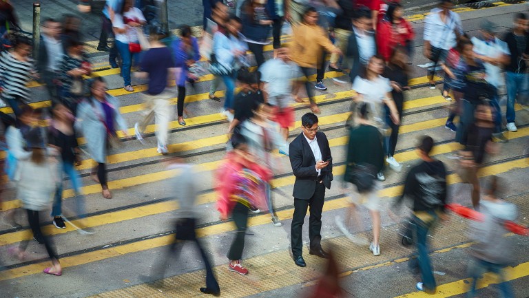 High angle view of businessman using smart phone amidst crowd. Professional is standing on busy street